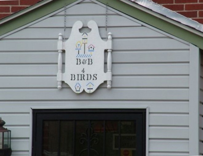 Exterior view of the B&B 4 Birds facility, showing a white hanging sign with the store name 'B&B 4 Birds' flanked by birdhouse icons.